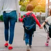 Μητέρα κρατάει τα 3 της παιδιά από το χέρι που πάνε σχολείο φορώντας τσάντες