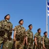 Στρατιώτες, φαντάροι σε στάση προσοχής με φόντο την ελληνική σημαία