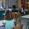 Μαθητές σε θρανία σε σχολείο με δασκάλα στο βάθος
