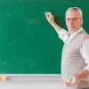 Καθηγητής δείχνει με κιμωλία σε πίνακα κοιτάζοντας προς την κάμερα