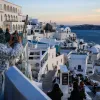 Γυναίκα τραβάει φωτογραφία τη Σαντορίνη κατά το ηλιοβασίλεμα, για το πρόγραμμα Τουρισμός για Όλους 2026-2027.