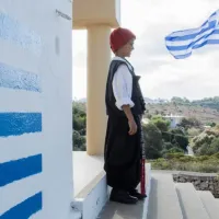 Μαθητής σε σχολείο με παραδοσιακή στολή και την Ελληνική σημαία