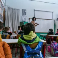 Σχολική τάξη, μαθητές σε θρανία και στο βάθος η δασκάλα τους μιλάει