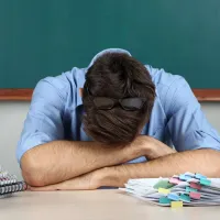 Δάσκαλος κουρασμένος ξαπλώνει πάνω στα χέρια του στην έδρα 