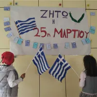 Μαθητές με ελληνική σημαία κοιτάνε πινακίδα που γράφει ζήτω η 25η Μαρτίου