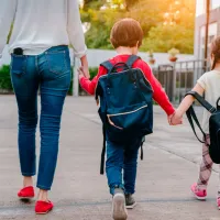 Μητέρα κρατάει τα 3 της παιδιά από το χέρι που πάνε σχολείο φορώντας τσάντες