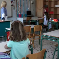 Μαθητές σε θρανία σε σχολείο με δασκάλα στο βάθος
