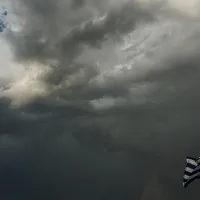 Μαύρα σύννεφα στον ουρανό πίσω από μια ελληνική σημαία
