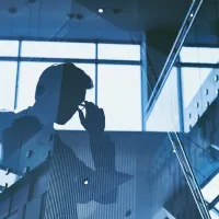 Άνδρας με κοστούμι και γυαλιά σε φόντο τζαμαρίας που φαίνεται μόνο η σκιά του
