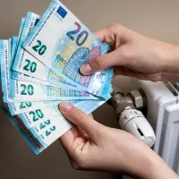 Χέρια μετράνε χρήματα για το επίδομα θέρμανσης δίπλα σε καλοριφέρ