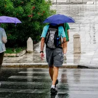 Πολίτες με ομπρέλες σε βρεγμένο δρόμο κατά τη διάρκεια ανοιξιάτικης κακοκαιρίας με βροχές και άστατο καιρό