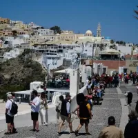 Τουρίστες περπατούν σε σοκάκι ελληνικού νησιού με φόντο παραδοσιακά λευκά σπίτια και εκκλησία με γαλάζιο τρούλο, για το πρόγραμμα Τουρισμός για Όλους