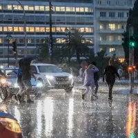 Κόσμος με ομπρέλες σε κακό καιρό στο Σύνταγμα περνάει το δρόμο ενώ έχει καταιγίδα