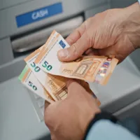 Ηλικιωμένος συνταξιούχος μετράει τη σύνταξή του σε χρήματα μπροστά από τράπεζα