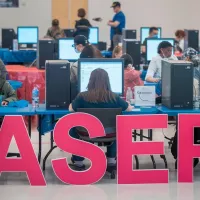 Άνθρωποι κάθονται σε κομπιούτερ με το λογότυπο του ΑΣΕΠ στα αγγλικά να βρίσκεται μπροστά τους