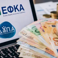 Λογότυπο ΕΦΚΑ και ΔΥΠΑ σε υπολογιστή και στο πληκτρολόγιο φαίνονται χρήματα