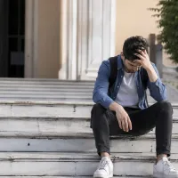 Πτυχιούχος με σκυμμένο κεφάλι μπροστά από Πανεπιστήμιο
