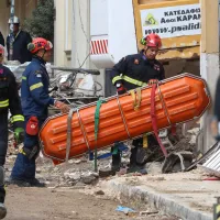 Άνδρες της ΕΜΑΚ μεταφέρουν φορείο για τους νεκρούς στο κτήριο της Πλάκας που έγινε έκρηξη