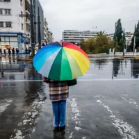 Άτομο κρατά πολύχρωμη ομπρέλα ενώ βρέχει στο Σύνταγμα μπροστά από τη Βουλή