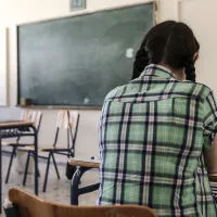 Μαθήτρια με πλάτη στην κάμερα κοιτάζει δασκάλα την ώρα που κάνει μάθημα στην έδρα της τάξης
