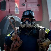 Πυροσβέστης με μάνικα και πίσω του όχημα της Πυροσβεστικής