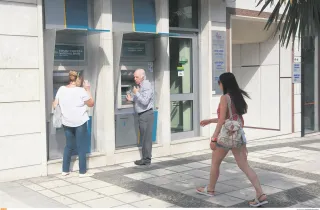 Ηλικιωμένος άνδρας και γυναίκα πραγματοποιούν συναλλαγές σε εξωτερικά ATM της Εθνικής Τράπεζας στο πεζοδρόμιο, ενώ μια κοπέλα περνάει από μπροστά.