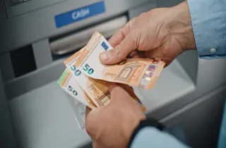 Ηλικιωμένος συνταξιούχος μετράει τη σύνταξή του σε χρήματα μπροστά από τράπεζα