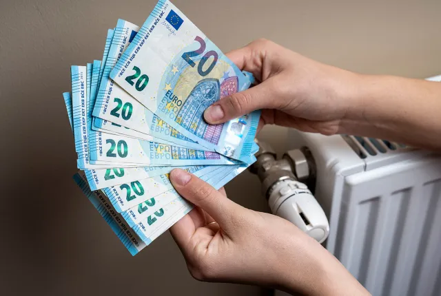 Χέρια μετράνε χρήματα για το επίδομα θέρμανσης δίπλα σε καλοριφέρ