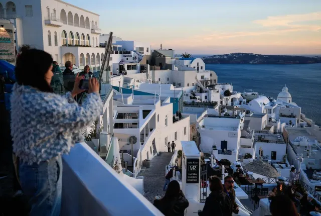 Γυναίκα τραβάει φωτογραφία τη Σαντορίνη κατά το ηλιοβασίλεμα, για το πρόγραμμα Τουρισμός για Όλους 2026-2027.