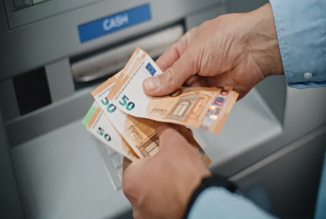 Ηλικιωμένος συνταξιούχος μετράει τη σύνταξή του σε χρήματα μπροστά από τράπεζα