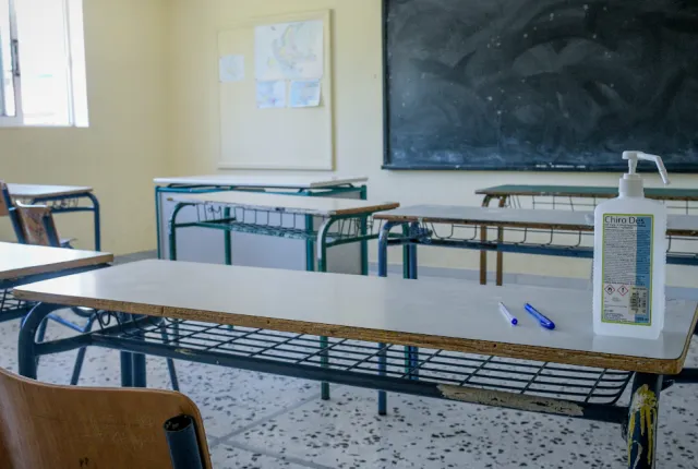 Αίθουσα σχολείου με άδεια θρανία, πίνακα και αντισηπτικό επάνω σε θρανίο