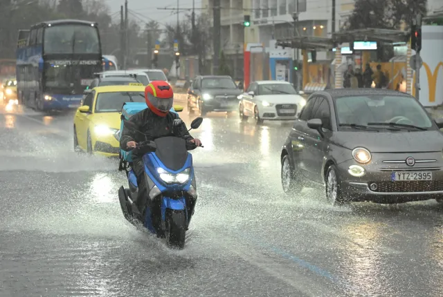 Αυτοκίνητα και μηχανές στον δρόμο ενώ ρίχνει δυνατή βροχή και ο δρόμος έχει νερά