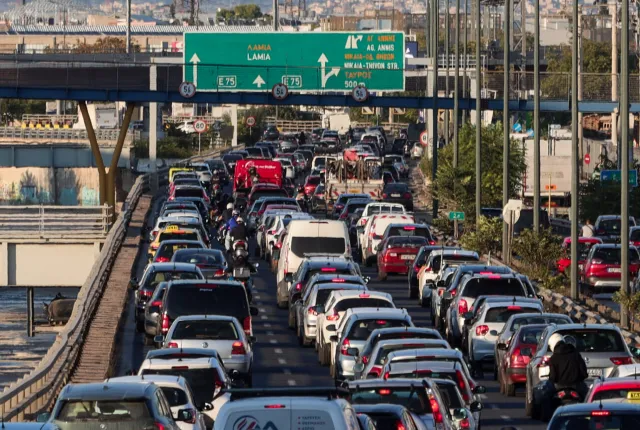 Φωτογραφία αυτοκινήτων σε ελληνικό δρόμο εν κινήσει, με φόντο αστικό τοπίο, που σχετίζεται με θέματα τελών κυκλοφορίας και ελέγχων οχημάτων από την ΑΑΔΕ