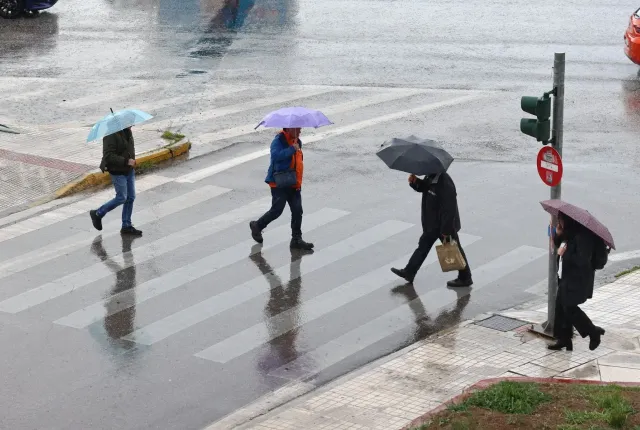 Βροχές και καταιγίδες στην Αθήνα με κόσμο να περνάει τον δρόμο με ομπρέλες