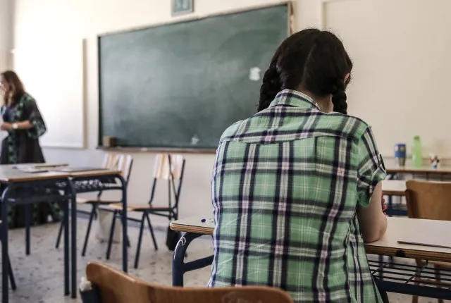 Μαθήτρια με πλάτη στην κάμερα κοιτάζει δασκάλα την ώρα που κάνει μάθημα στην έδρα της τάξης