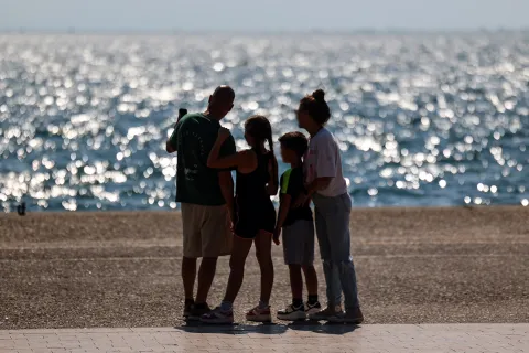 Οικογένεια που θα πάρει το έκτακτο επίδομα παιδιού κοιτάζει τη θάλασσα αγκαλιά