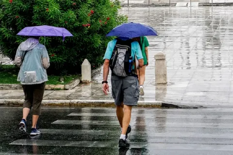 Πολίτες με ομπρέλες σε βρεγμένο δρόμο κατά τη διάρκεια ανοιξιάτικης κακοκαιρίας με βροχές και άστατο καιρό