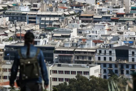 Γυναίκα κοιτάει πανοραμικά τα σπίτια στην Αθήνα από λόφο