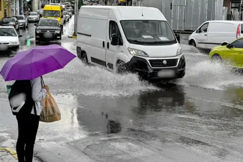 Γυναίκα περπατάει με ομπρέλα εν μέσω κακοκαιρίας ενώ αμάξια είναι σε βρεγμένο δρόμο