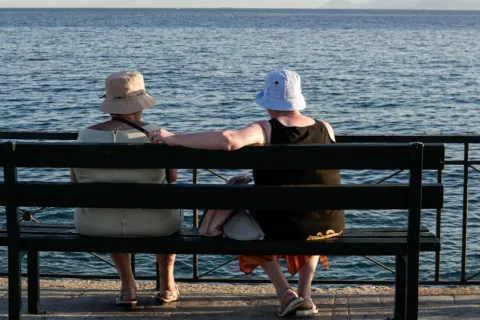 Γυναίκες συνταξιούχοι κάθονται σε παγκάκι και κοιτάνε τη θάλασσα το καλοκαίρι