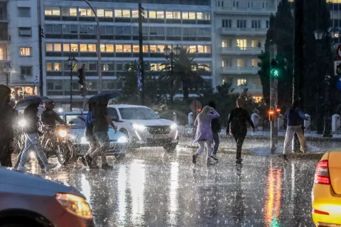 Κόσμος με ομπρέλες σε κακό καιρό στο Σύνταγμα περνάει το δρόμο ενώ έχει καταιγίδα