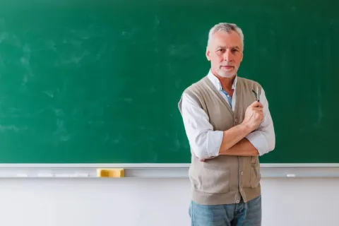 Εκπαιδευτικός μπροστά από πίνακα κοιτάζει την κάμερα ενώ περιμένει το άνοιγμα του ΟΠΣΥΔ