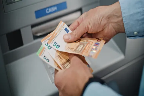 Ηλικιωμένος συνταξιούχος μετράει τη σύνταξή του σε χρήματα μπροστά από τράπεζα