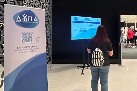 Γυναίκα περπατάει σε διάδρομο με το λογότυπο της ΔΥΠΑ