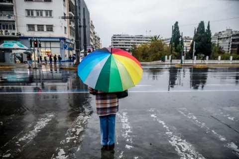 Άτομο κρατά πολύχρωμη ομπρέλα ενώ βρέχει στο Σύνταγμα μπροστά από τη Βουλή